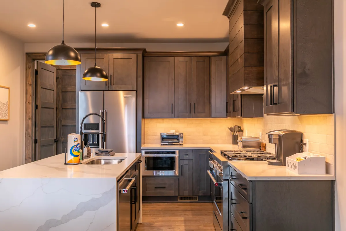 A stylish kitchen featuring a central island with ample seating, sleek stainless steel appliances, pendant lighting, and dark cabinetry. The open layout allows for seamless interaction with the living and dining areas, creating a social hub for gatherings.