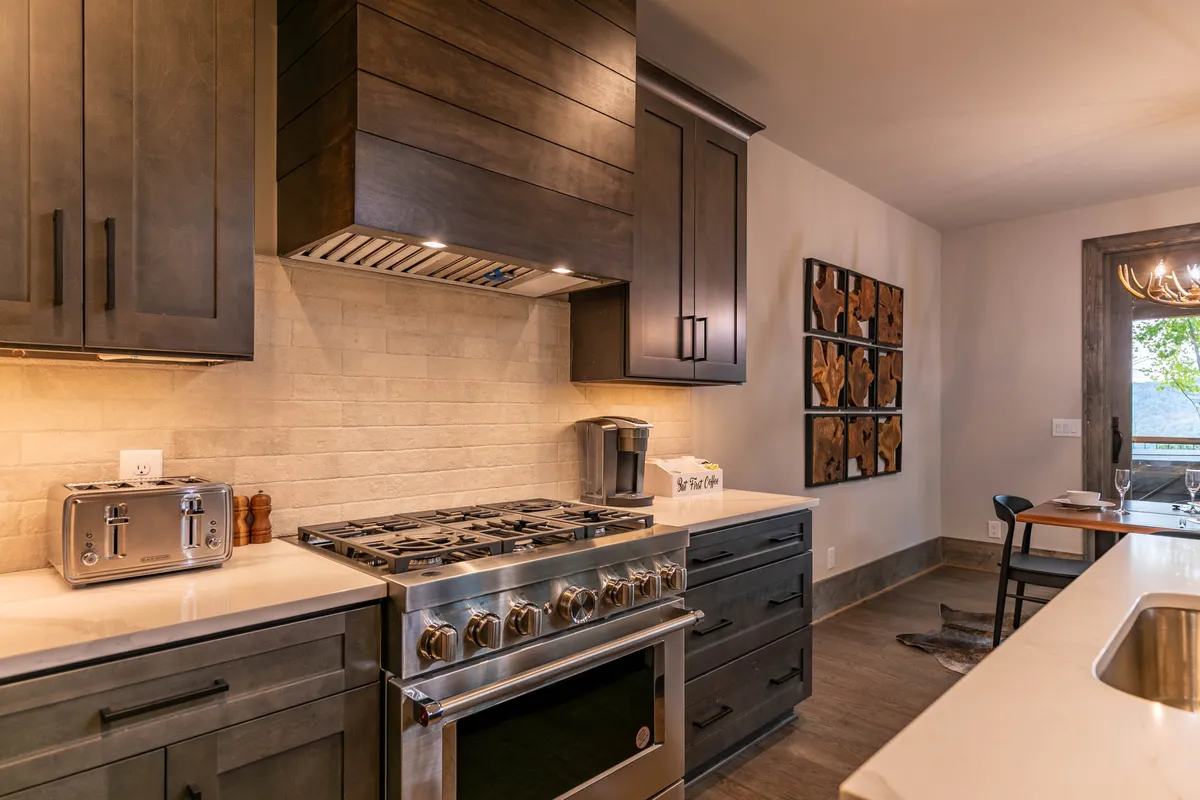 A close-up view of the kitchen’s sleek stainless steel gas range, dark cabinetry, textured backsplash, and modern wood artwork. The setup suggests a well-equipped space for culinary adventures and effortless meal prep.