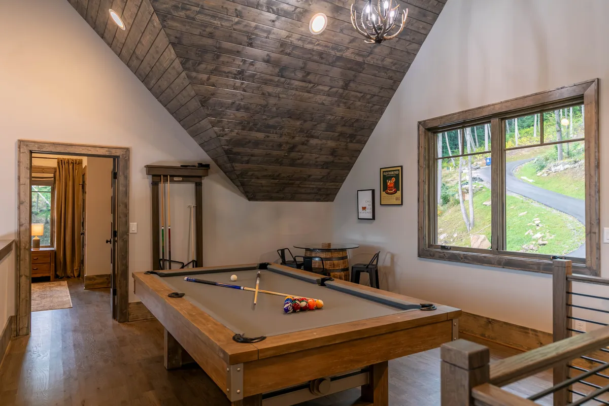 A lively entertainment and game area featuring a pool table set against wooden walls. A large window brings in natural light and hints at mountain scenery, while a chandelier adds a playful yet refined touch to the space. The room is perfect for friendly competitions and relaxed socializing.
