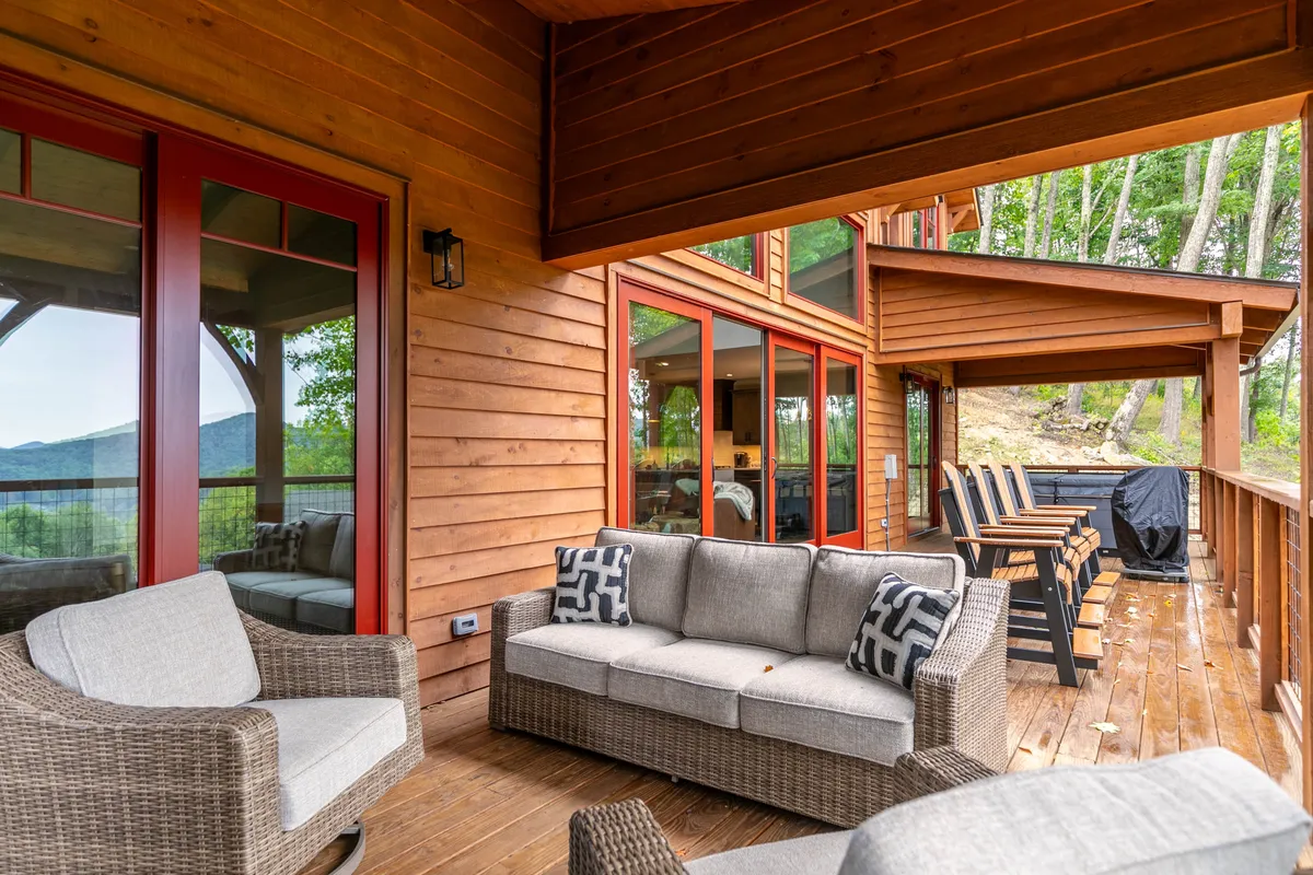 A welcoming wooden deck with comfortable seating, surrounded by lush greenery and large windows that hint at the indoor-outdoor flow. The space is ideal for relaxing, enjoying nature views, or sharing a meal after outdoor activities.
