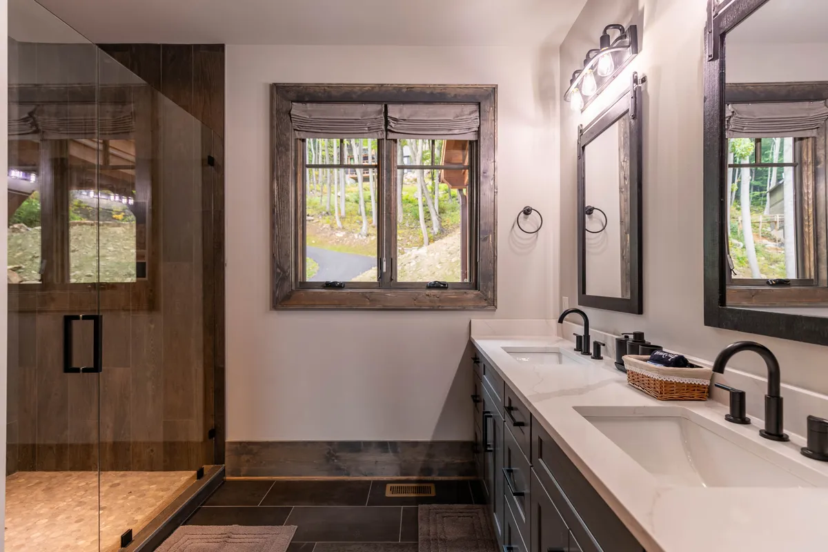 A spacious bathroom with dual sinks, large mirrors, and a window letting in soft morning light. The design is modern and tranquil, inviting guests to enjoy self-care routines in a refreshing space.