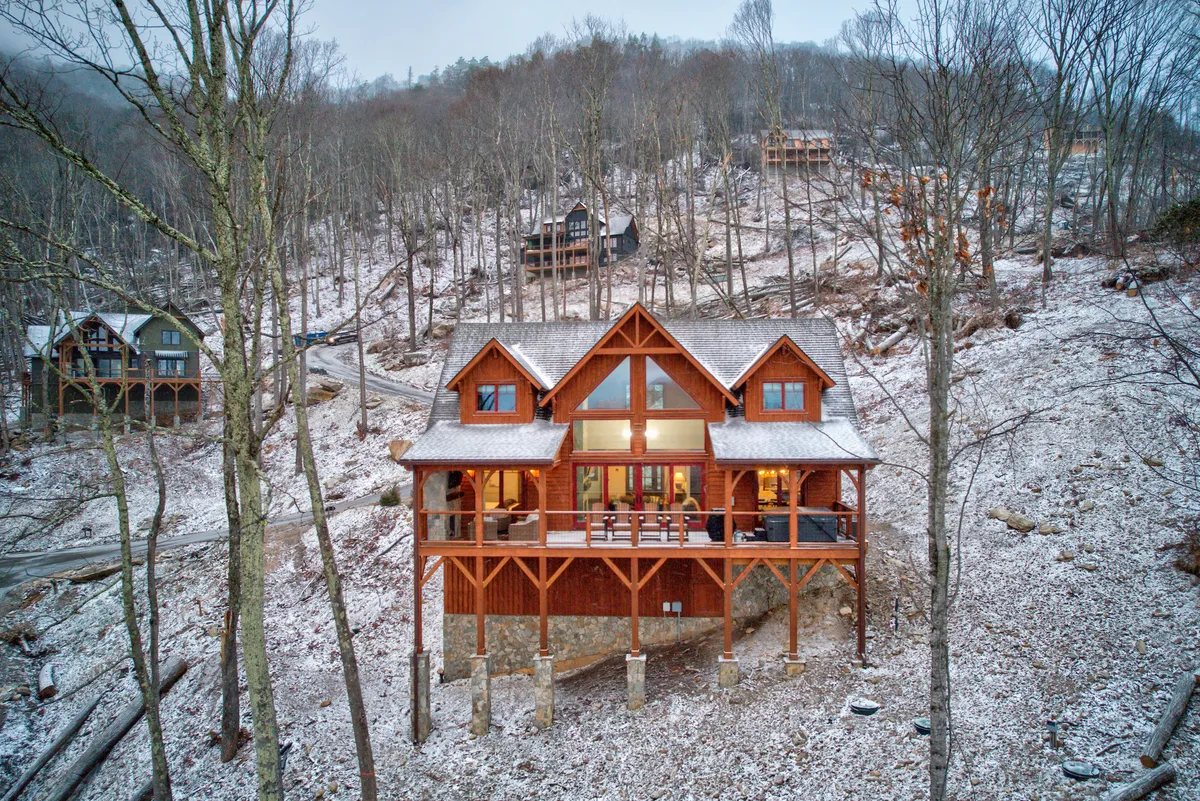 The cabin sits amidst a snowy landscape, its porch furnished for comfort and inviting relaxation. The snow-covered ground highlights the winter atmosphere, suggesting activities like snowshoeing, skiing, and cozy moments on the porch with a warm drink.