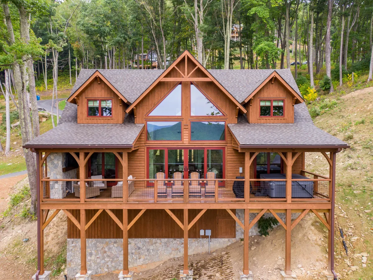This image shows the wooden balcony of the cabin, accentuated by large windows, a stone foundation, and surrounded by trees. The balcony is spacious, providing ample room for outdoor seating and gatherings. The natural setting emphasizes the property's connection to the surrounding landscape and offers a tranquil spot to enjoy with friends or family.
